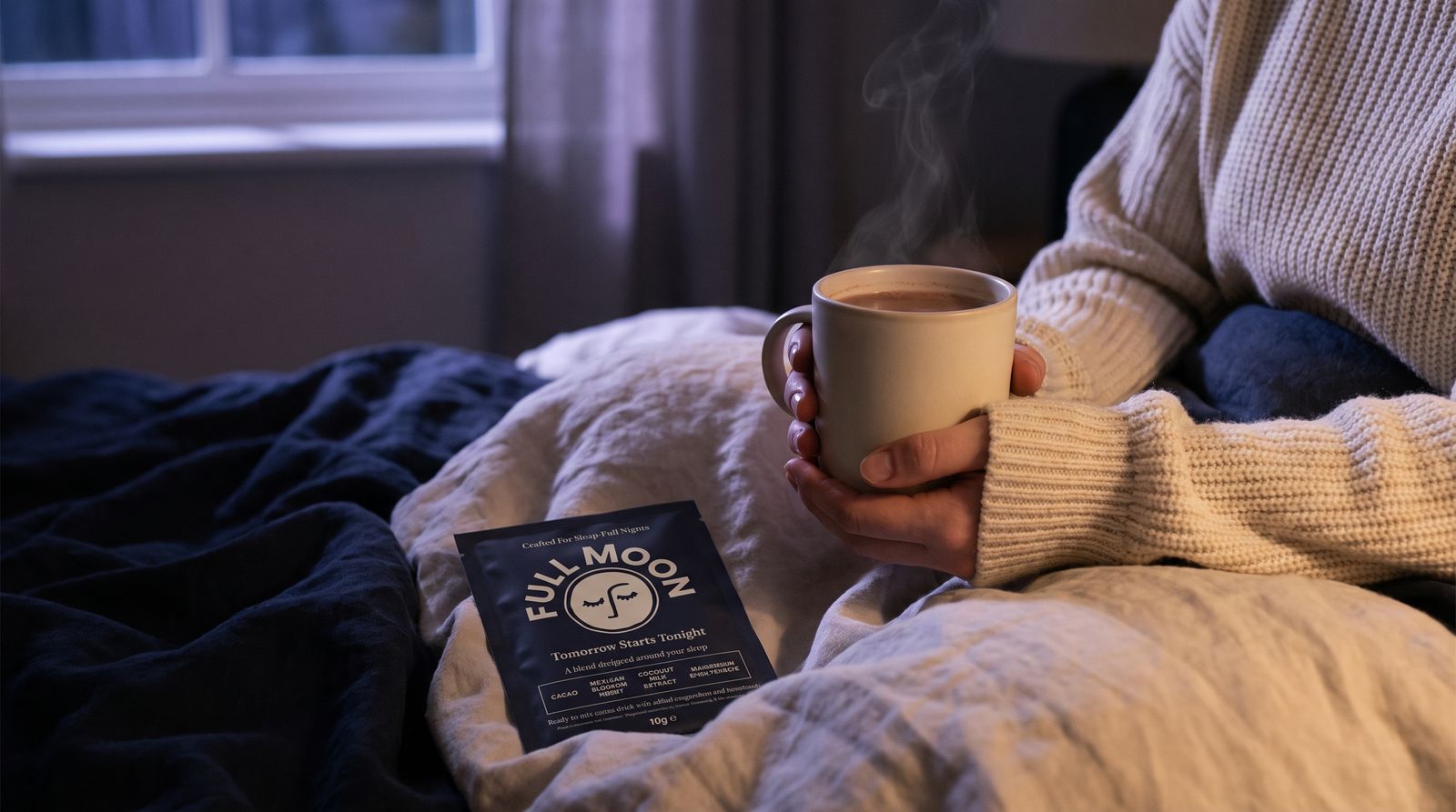 A steaming mug of Full Moon hot cacao held in bed at night